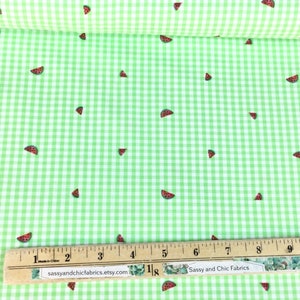 K&ouml;nnte beinhalten: Gr&uuml;n-wei&szlig;es Vichy-Gewebe mit verstreuten Wassermelonen-Scheibenmustern. Ein Holzlineal mit Zentimetermessungen liegt auf dem Stoff. Der Text "Sassy and Chic Fabrics" ist sichtbar.