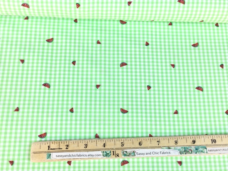 K&ouml;nnte beinhalten: Gr&uuml;n-wei&szlig;es Vichy-Gewebe mit verstreuten Wassermelonen-Scheibenmustern. Ein Holzlineal mit Zentimetermessungen liegt auf dem Stoff. Der Text "Sassy and Chic Fabrics" ist sichtbar.