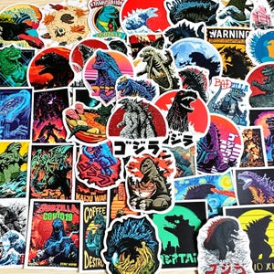 May include: A collection of numerous vinyl stickers featuring various artistic depictions of Godzilla, including silhouettes, colourful illustrations, and scenes with Japanese text, ramen bowls, and cityscapes, all layered together in a dense collage.