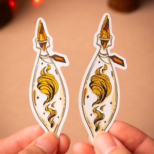 May include: Two gold and white sticker designs of a potion bottle with a swirling golden liquid inside. The bottle has a cork stopper and a tag hanging from the neck.
