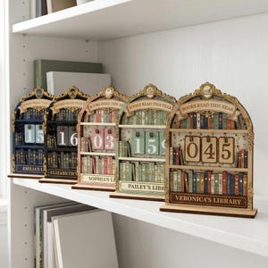 May include: Wooden bookshelf-shaped book trackers with the text "BOOKS READ THIS YEAR" at the top. Each shelf displays a different number, such as 15, 16, 03, 15, and 045. The shelves are personalized with names like "EMILIA'S LIBRARY" and "VERONICA'S LIBRARY".