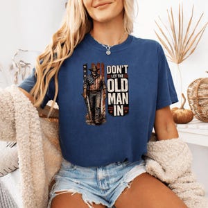 Peut inclure: T-shirt bleu marine avec un motif d'un homme portant un chapeau de cowboy et un drapeau américain. Le texte dit "DON'T LET THE OLD MAN IN". Le t-shirt est de style décontracté.