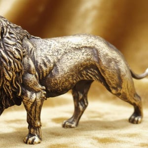 May include: A bronze-colored lion figurine with a detailed mane and muscular build. The lion is depicted in a walking pose, showcasing its powerful stance. The sculpture has a textured surface and is set against a golden background.