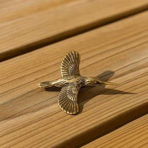 Peut inclure: Une sculpture d'oiseau en bronze aux ailes déployées, posée sur une surface en bois. La sculpture présente des détails de plumes et un long bec, capturant l'oiseau en plein vol. Un objet décoratif.