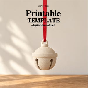 以下が含まれることがあります： 赤いリボンで吊るされたベージュのベル。上部には「ceramixis」、「Printable TEMPLATE」、「digital download」という文字が記載されています。ベルは滑らかでマットな質感で、クラシックな丸みを帯びた形状をしており、底面には縦型のスリットが入っています。