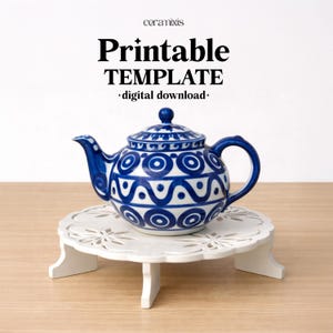 Puede incluir: Una tetera de cerámica azul y blanca con un patrón decorativo se encuentra sobre un soporte blanco de tres patas. La tetera tiene un pico y un asa curvados. La imagen incluye el texto "Printable TEMPLATE - digital download-".
