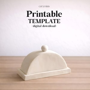 Puede incluir: Una mantequera cremosa en forma de cúpula con un pequeño asa esférica en la parte superior. El plato se asienta sobre una base rectangular. Las palabras "Printable TEMPLATE - digital download -" están impresas en negro.