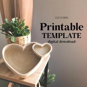 Può includere: Modello stampabile per un piatto in ceramica a forma di cuore con un piatto più piccolo a forma di cuore all'interno. Il modello è per un download digitale. L'immagine mostra il piatto su uno scaffale di legno.