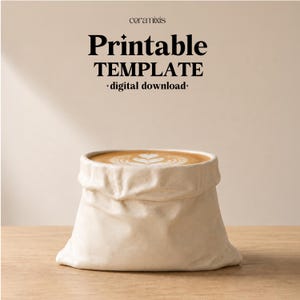 Pode incluir: Uma caneca de cerâmica em forma de saco de papel amarrotado cheia de café com latte art. O texto acima diz ceramixis Printable TEMPLATE digital download. A caneca tem um acabamento mate em branco sujo sobre uma superfície de madeira.
