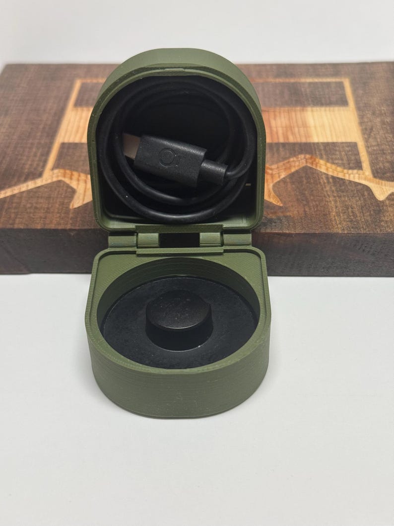 May include: A green, hinged, plastic case with a black charging cable inside. The case has a black button on the top.