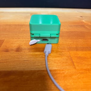 May include: A small, green, cube-shaped device with a white button and a USB-C port on the side. A grey cable is plugged into the port.