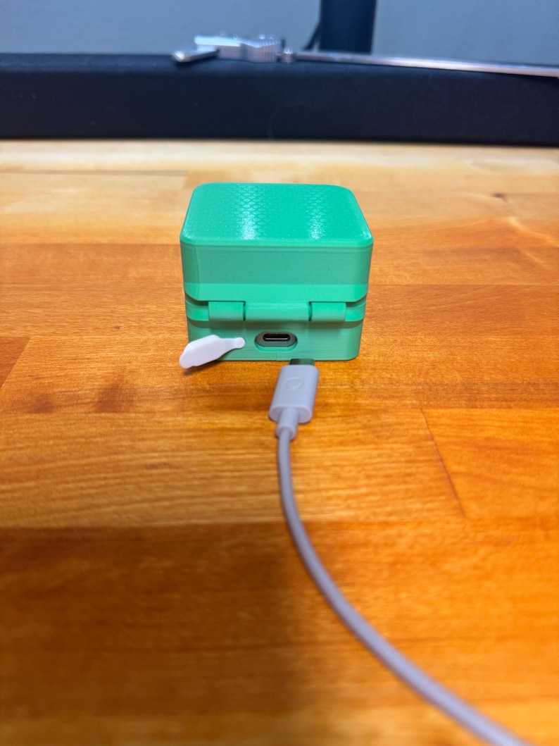 May include: A small, green, cube-shaped device with a white button and a USB-C port on the side. A grey cable is plugged into the port.