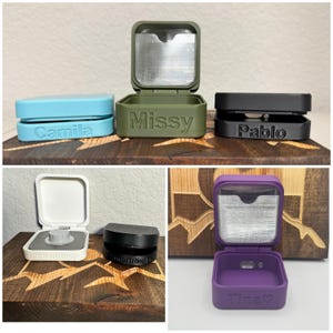 May include: Four small, square, hinged boxes with clear lids. The boxes are in different colours: light blue, green, black, and purple. Each box has a name engraved on the front: Camila, Missy, Pablo, and Tina.