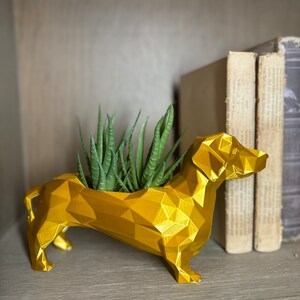 May include: A gold geometric dachshund planter with a succulent plant inside. The planter is sitting on a wooden shelf.