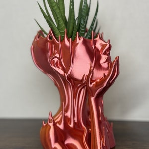 May include: A copper-colored, abstract, human-shaped planter with a succulent plant growing inside.