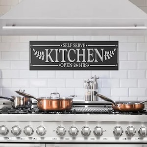 May include: A contemporary kitchen featuring stainless steel appliances, including a range, oven, and microwave. A white range hood is above the range. A black sign that says "SELF SERVE KITCHEN OPEN 24 HRS" hangs above the range.