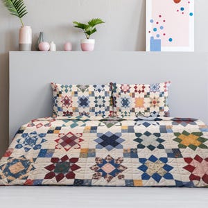 May include: A bed with a colorful quilt and two matching pillowcases. The quilt features a repeating pattern of star-like shapes in shades of blue, red, yellow, and cream. The bed is against a gray wall with decorative items on a shelf.
