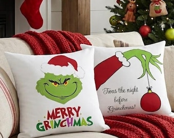Peut inclure: Deux coussins carrés blancs avec des motifs sur le thème du Grinch. L'un affiche le visage du Grinch portant un bonnet de Père Noël avec le texte Merry Grinchmas. L'autre montre une main verte tenant une boule rouge avec le texte Twas the night before Grinchmas.