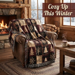 May include: A woven throw blanket featuring a patchwork pattern of pine trees and snowflakes in shades of burgundy, black, and tan, draped over a brown leather armchair. The text "Cozy Up This Winter" is displayed in the upper right corner.