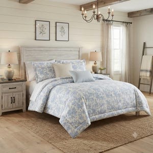 May include: A bed featuring a white and blue floral toile comforter, two matching floral pillow shams, a solid cream square throw pillow, and a rectangular light blue striped accent pillow, all arranged on a wooden bed frame with a headboard.