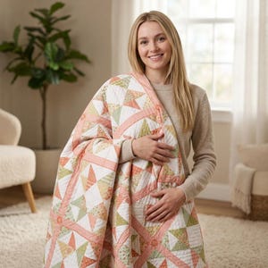 May include: A quilted blanket featuring a geometric star pattern in shades of soft peach, sage green, and white. The fabric displays a mix of solid colors and small floral prints, with peach-colored sashing separating the square quilt blocks.