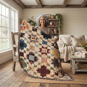 May include: A woven throw blanket featuring a patchwork star pattern in muted tones of burgundy, navy blue, cream, and sage green. The blanket has a fringed edge and is constructed from multiple square fabric blocks arranged in a geometric design.