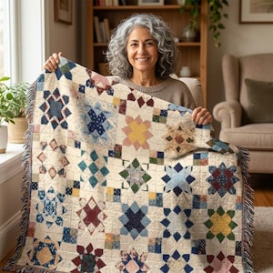 May include: A cream-coloured throw blanket with a patchwork design featuring star and diamond patterns in various colours, including blue, red, and yellow. The blanket has a fringed edge and a woven texture, ideal for adding warmth and style to any living space.