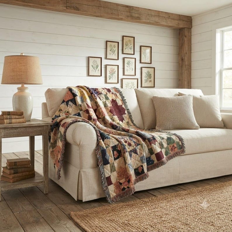 May include: A woven throw blanket featuring a multi-colored patchwork pattern with floral and geometric motifs draped over a cream-colored sofa. The blanket has a fringed edge and displays a variety of muted earth tones including red, blue, and tan.