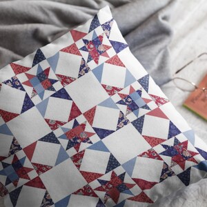 Op de afbeelding: Een vierkant sierkussen met een herhalend quiltpatroon van achtpuntige sterren in tinten rood, marineblauw en lichtblauw op een witte achtergrond. De stof toont ingewikkelde bloemmotieven en geometrische prints binnen de stervormen.