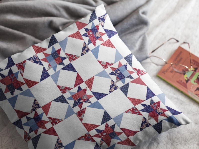 Op de afbeelding: Een vierkant sierkussen met een herhalend quiltpatroon van achtpuntige sterren in tinten rood, marineblauw en lichtblauw op een witte achtergrond. De stof toont ingewikkelde bloemmotieven en geometrische prints binnen de stervormen.