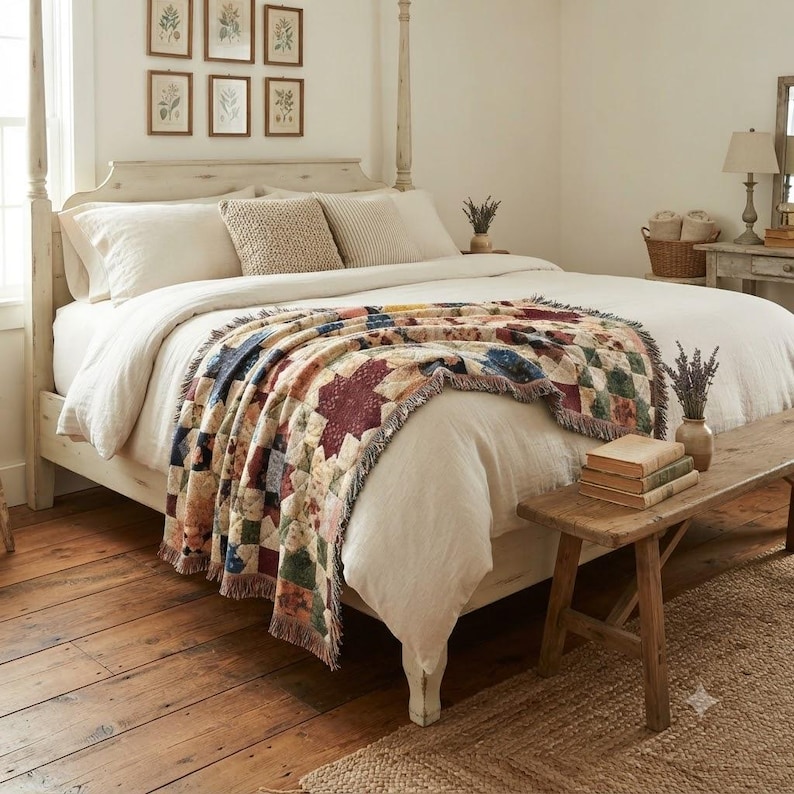 May include: A cream-colored bed with a wooden frame, topped with a white duvet and a woven throw blanket featuring a multi-colored patchwork star pattern. The bed includes two cream pillows and a textured beige accent pillow, with a wooden bench.