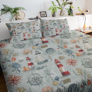 May include: A light blue nautical-themed bedding set featuring lighthouses, sailboats, anchors, seashells, and coral. The pattern includes red, white, and blue elements. The set includes a duvet cover and two pillowcases.