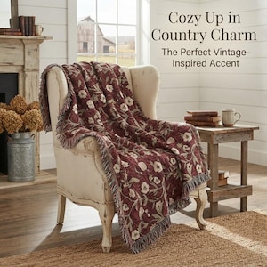May include: A cream-colored wingback chair draped with a deep red woven throw blanket featuring a white floral pattern and fringed edges. The text "Cozy Up in Country Charm The Perfect Vintage-Inspired Accent" is visible in the upper right corner.
