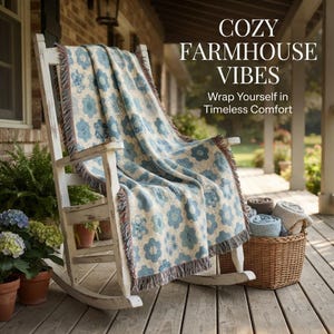 May include: A white wooden rocking chair draped with a woven throw blanket featuring a blue and cream floral pattern and fringed edges. The text COZY FARMHOUSE VIBES Wrap Yourself in Timeless Comfort is visible. A wicker basket holds folded blankets.