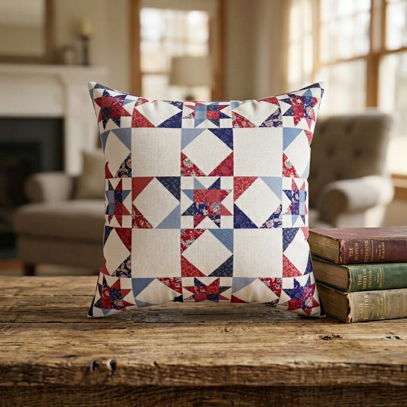 Op de afbeelding: Een vierkant sierkussen met een patchwork quiltontwerp met een herhalend sterpatroon. De stof toont een kleurenpalet van rood, wit en blauw, met bloemen- en geometrische prints verwerkt in de stervormen en de effen witte vierkanten.