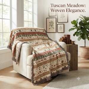 May include: A woven throw blanket featuring horizontal stripes with floral and botanical patterns in shades of terracotta, sage green, and cream. The blanket has a fringed edge and is draped over a cream-colored armchair. Text reads: Tuscan Meadow: Woven Elegance.