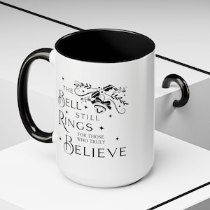 May include: White ceramic mug with a black interior and handle. The mug features the text "The Bell Still Rings For Those Who Truly Believe" in black, along with a decorative bell and holly design. A festive holiday-themed mug.