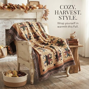 May include: A woven throw blanket featuring a repeating star pattern in shades of tan, brown, green, and burgundy, draped over a distressed white wooden chair. The text COZY. HARVEST. STYLE. Wrap yourself in warmth this Fall. is visible.