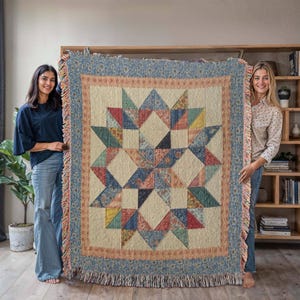 May include: A large, square quilt with a starburst pattern. The quilt features a cream-coloured centre with a geometric star design in various colours, including blue, red, and yellow. The border is a floral pattern in blue and cream, with a fringed edge.