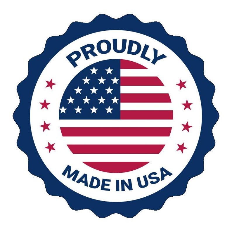 May include: A circular badge with a scalloped dark blue border featuring the text PROUDLY MADE IN USA in dark blue capital letters. The center contains a circular United States flag graphic surrounded by eight small red stars on a white background.