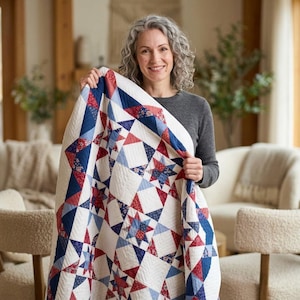 May include: A patchwork quilt featuring a geometric star pattern in shades of red, white, and navy blue. The design incorporates solid colors and small floral prints arranged in repeating triangular and square blocks with visible stitching.