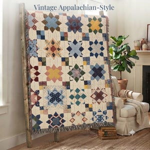 Könnte beinhalten: Eine gewebte Wohndecke mit einem wiederkehrenden Sternenmuster in Blau-, Gelb-, Rot- und Grüntönen auf cremefarbenem Grund. Der Text "Vintage Appalachian-Style" steht oben. Die Decke hat einen Fransenrand und hängt über einer Holzleiter.
