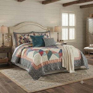 May include: A bed featuring a patchwork quilt with a star pattern in shades of red, blue, and cream, bordered by a dark floral print. The bedding includes a solid teal square pillow, a smaller floral accent pillow, and a cream-coloured knit throw.