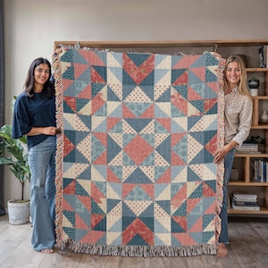 May include: A woven throw blanket with a geometric star pattern in shades of blue, red, and cream. The blanket has a fringed edge and is held up by two people. The design features triangles and diamond shapes.