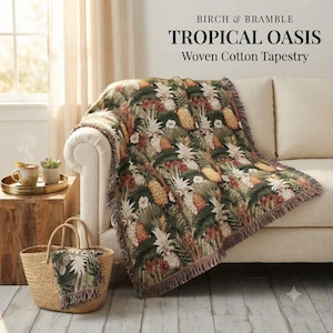 May include: A woven cotton tapestry titled Birch & Bramble Tropical Oasis featuring a repeating pattern of pineapples, tropical leaves, and flowers in shades of green, gold, and brown with fringed edges, draped over a light-colored sofa.