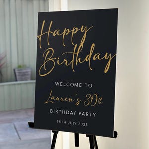 Könnte beinhalten: Schwarzes Schild mit goldfarbenem Text, der "Happy Birthday" lautet. Es heißt "Willkommen zu Laurens 30. Geburtstagsparty" am "15. Juli 2025". Das Schild wird auf einer schwarzen Staffelei präsentiert.