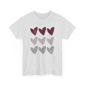 Könnte beinhalten: Ein hellgraues T-Shirt mit einem Design aus neun Herzen in Grautönen und Burgunderrot. Die Herzen haben die Worte "Einheit", "Liebe" und "Respekt" darin geschrieben.
