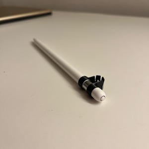 May include: A white stylus with a black and silver band and a black clip. The stylus is designed for use with a tablet or touchscreen device. The stylus is on a white surface.