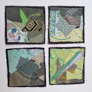 May include: Four square fabric coasters featuring layered patchwork designs in shades of green, blue, and white. Each coaster displays intricate hand-stitched embroidery, frayed edges, and a variety of floral, geometric, and solid textile patterns.