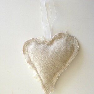 May include: A beige heart-shaped fabric ornament with a frayed edge and a white string for hanging.